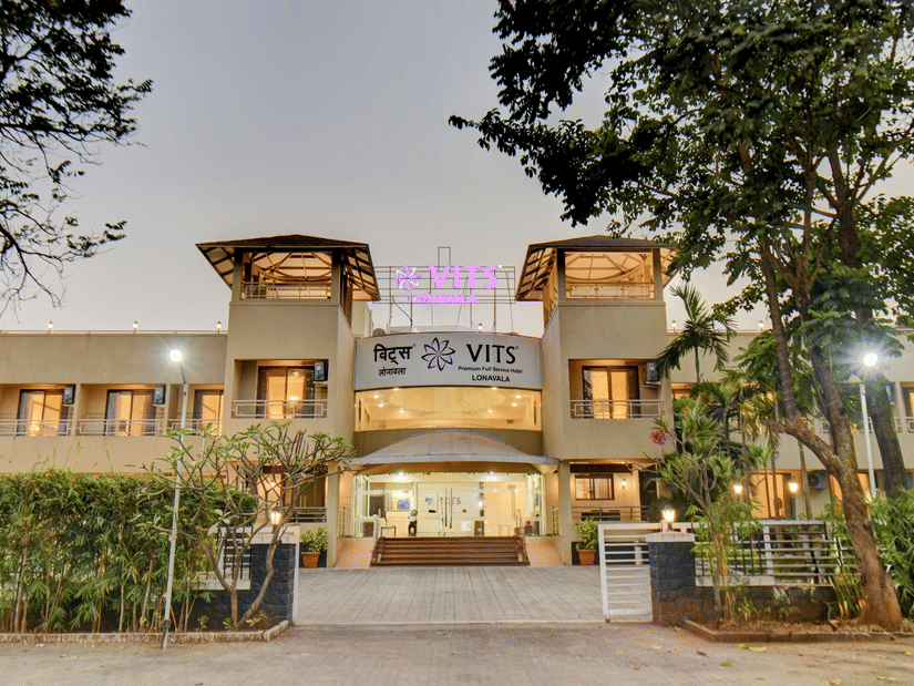 Main entrance of the hotel with welcoming exterior design at VITS Lonavala, surrounded by trees and seen during twilight hour.