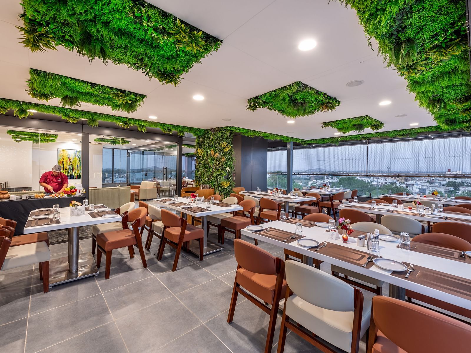A stylish restaurant with large windows, chic furniture, and greenery lime tree on the ceiling.