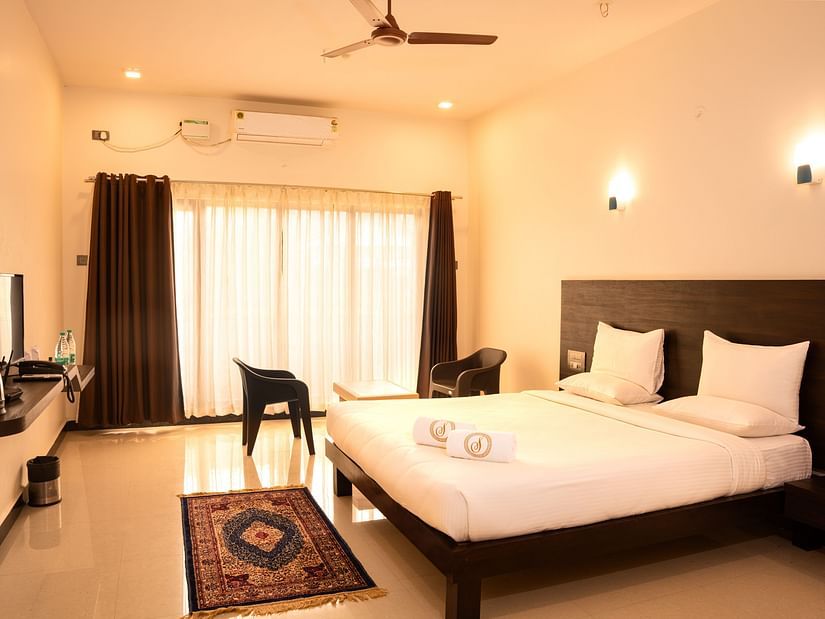 A deluxe ac room with a tv opposite a double bed at Mastiff Select Terrain, Dandel. The room also features a fan, a seating area with two chairs and a centre table, and a large window
