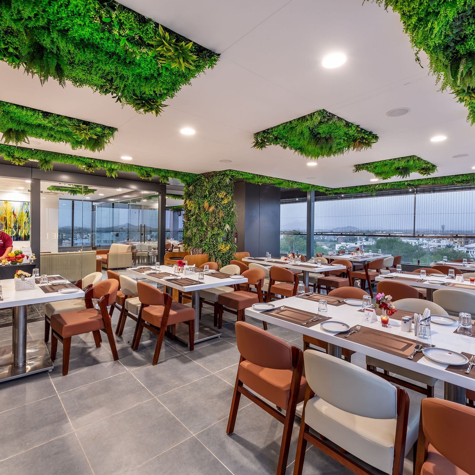 A stylish restaurant with large windows, chic furniture, and greenery lime tree on the ceiling.