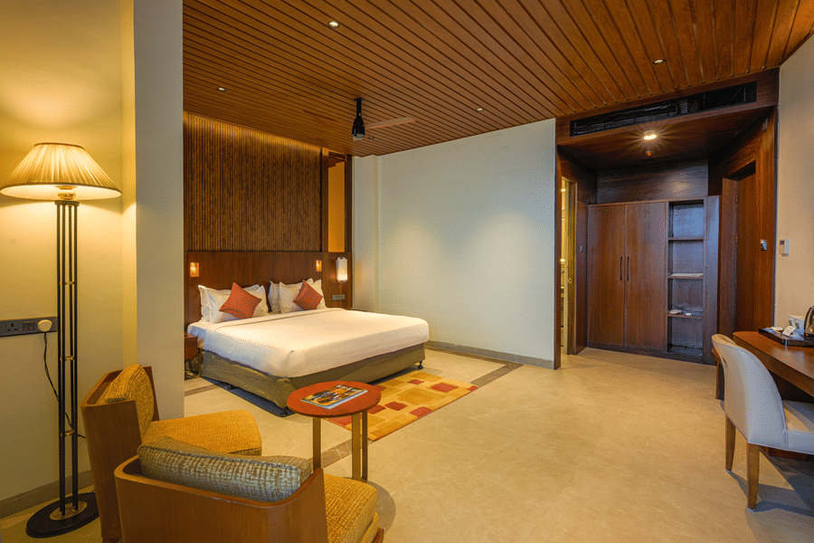 Spacious hotel bedroom with a king size bed, wooden ceiling, upholstered seating, bedside lighting and a large television.