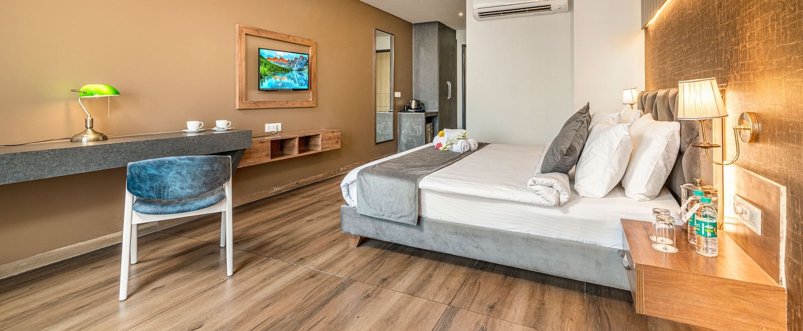 An image of the deluxe room with a bed, work desk and chair, flat screen TV, and warm lighting - DLS Ganga Bliss, Haridwar