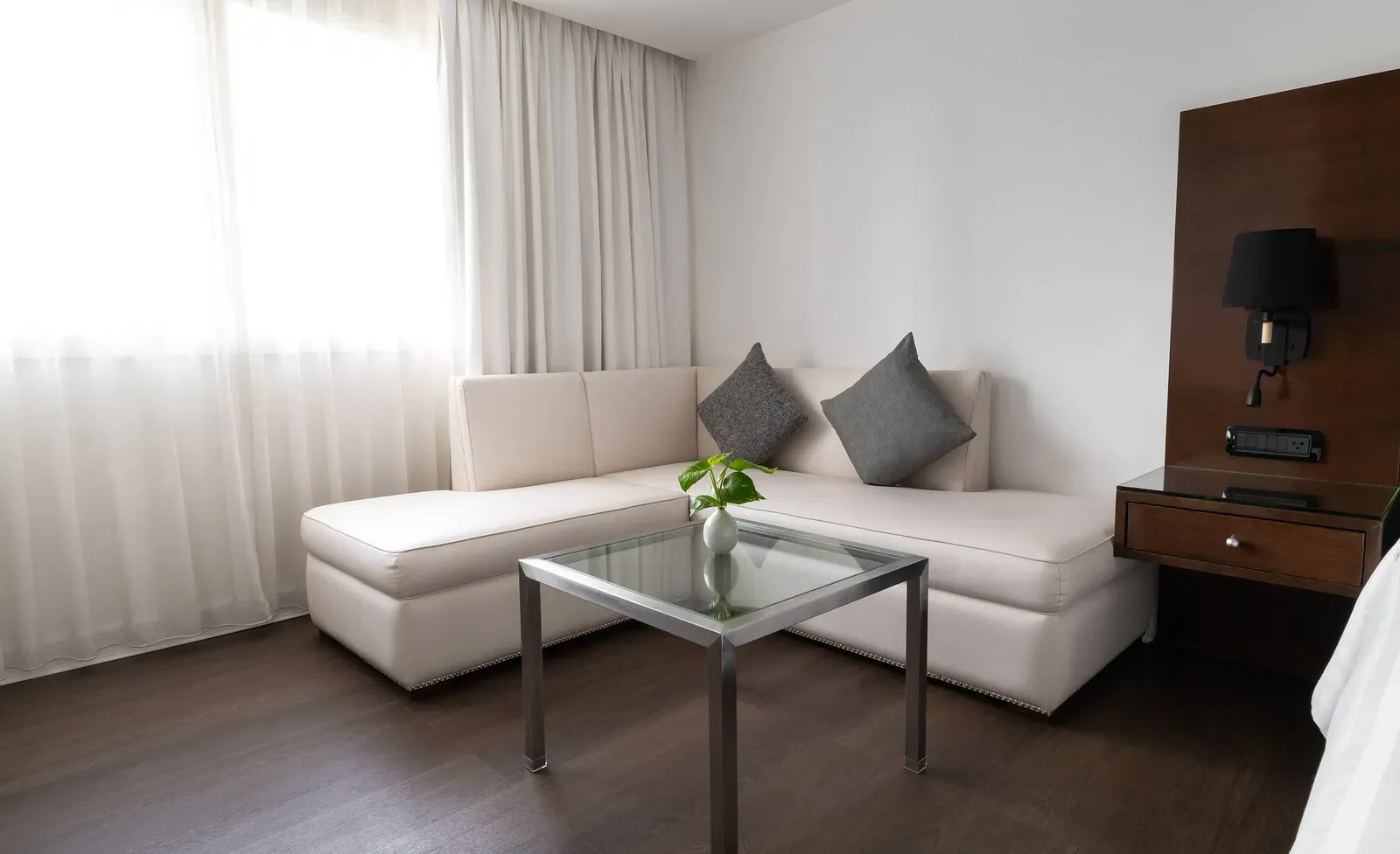 Elegant hotel seating area featuring cream sectional sofa, glass coffee table, grey cushions, and walnut entertainment unit with contemporary styling at Night Hotel Bangkok.