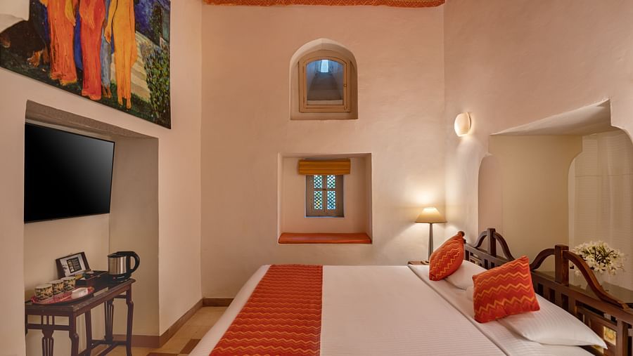 A room with a bed, a television, a small table, and a window with a built-in seat in Tijara Fort-Palace - 19th Century, Alwar.