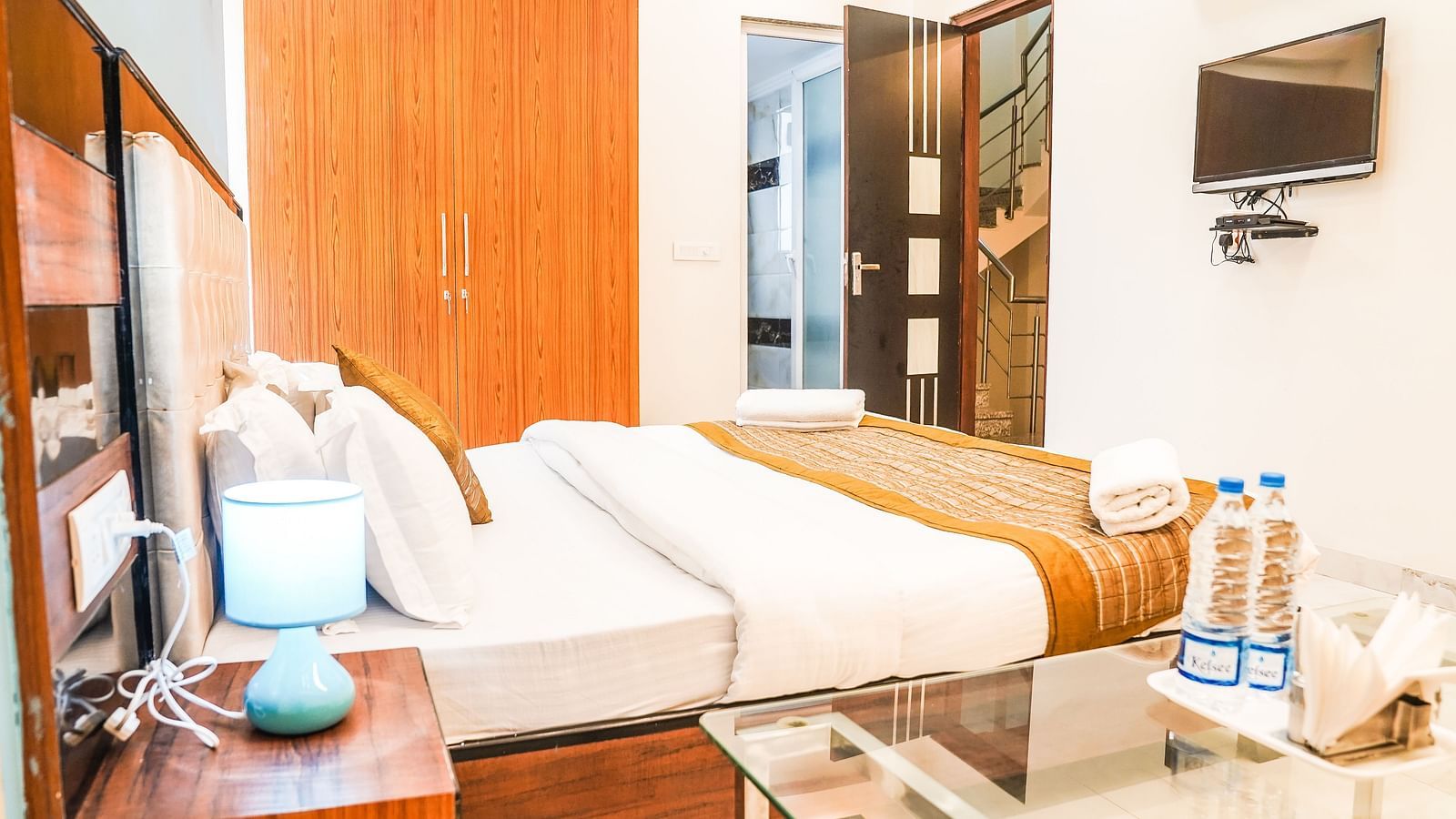 A well-lit room features a double bed with white and brown bedding, wooden furniture, and a television on the wall - Asian Suites Cyber Park, Gurgaon