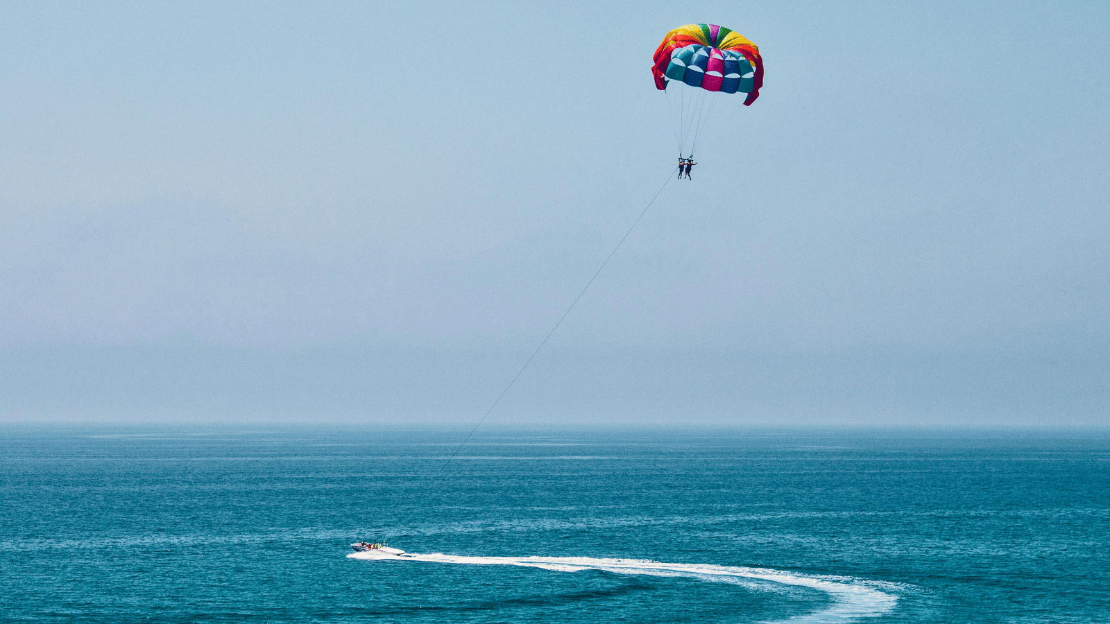 Parasailer soaring over the Sea and a motorboat creating a circular wake below in the sea.