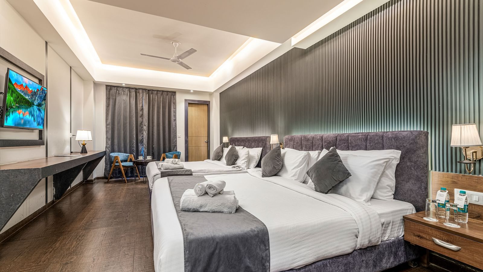 A mirror shot of a room at DLS Ganga Bliss, Haridwar with two king size beds facing a flat screen TV mounted on a wall