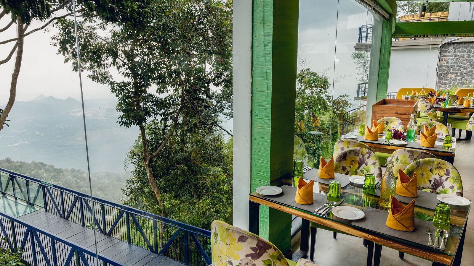 An image of a restaurant with seating arrangement and expansive glass window over looking the serene mountains - Great Trails Yercaud by GRT Hotels
