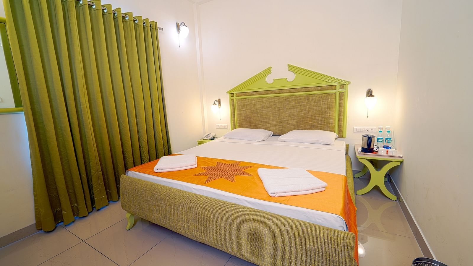 A hotel bedroom with a large double bed, green headboard, and green curtains, giving a cozy ambience at Greens Inn - Best Accommodation in Ramoji Film City.
