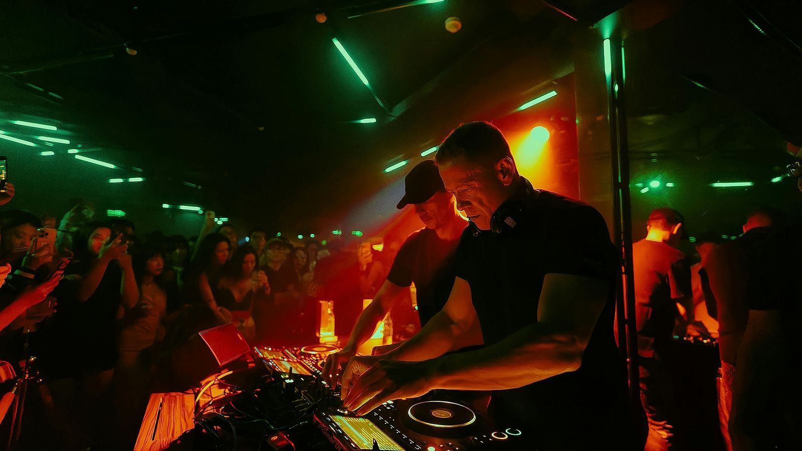 An overview of a club with the DJ mixing songs on a turntable and people dancing next to him.
