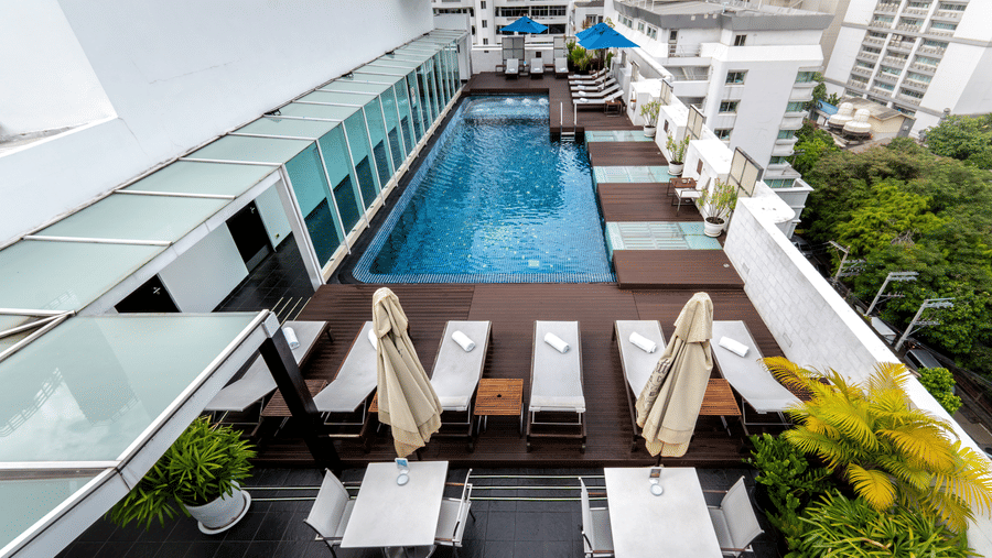 Aerial view of the rooftop swimming pool with loungers, potted plants and other high rise buildings and trees next to the hotel - Night Hotel Bangkok - one of the best Guest-Friendly Hotels Near Soi Cowboy, Bangkok.