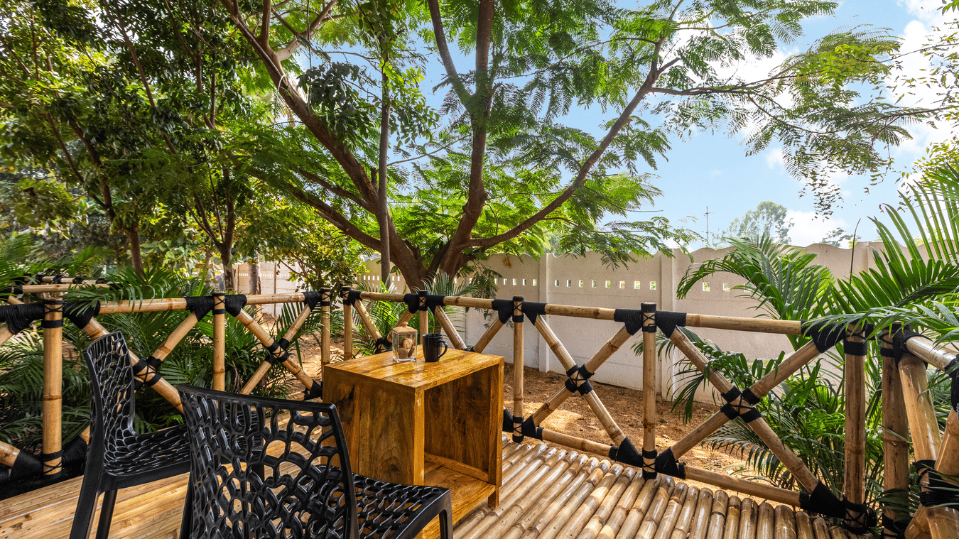 Outdoor balcony with bamboo railings and black wicker chairs overlooking lush trees - Nature Trails Ashoka Resort Hampi