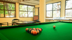 A close view of a billiard table with the balls racked, next to a wall of windows at an indoor playing area of Adamo The Village