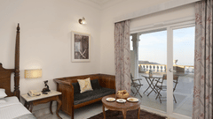 Deluxe Room with Balcony at Fateh Safari Resort, Kumbhalgarh featuring a seating area with sofa, centre table, a corner of the bed, bedside table, and chairs and tables on the balcony.