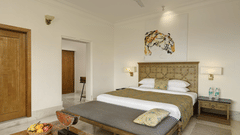 Bedroom of Valley View Suite with Jacuzzi at Fateh Safari Suites, Kumbhalgarh featuring double size bed, bedside table with electric lamps on either side, a sofa in front of the bed and then a centre table with fruits.