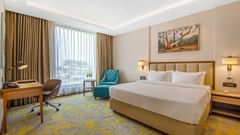 A room at Golden Tulip, Jalandar featuring a double size bed, a work desk and chair, and a sofa chair with centre table near a large window.