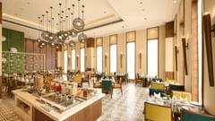 A bright and airy restaurant is furnished with tables and chairs in various colours, a buffet station, and stylish globe pendant lights hanging from the high ceiling. - Iris Sarovar Portico, Sector 85, Gurugram
