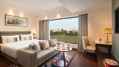 A suite at Sarovar Portico, Hanumangarh, with a double bed, a sofa, a window with a view, and a table.