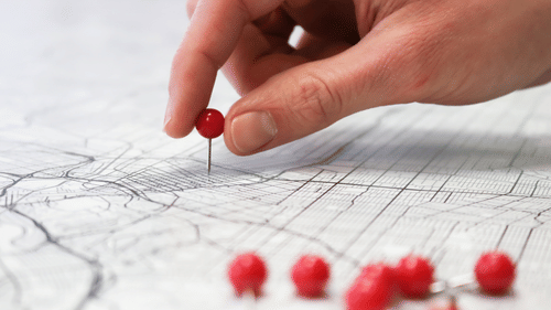 A close up of a person adding a red pin on a map with other pins kept on the side. One of facilities at Raj Park, Chennai include a travel desk to help guests navigate the city easily.