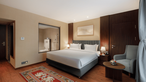 A spacious bedroom at Royal Tulip, Kathmandu, with a large bed and an en-suite bathroom visible through a window.