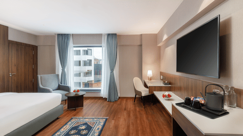 A spacious room at Royal Tulip, Kathmandu, with a large bed, seating area, desk, and flat-screen television.
