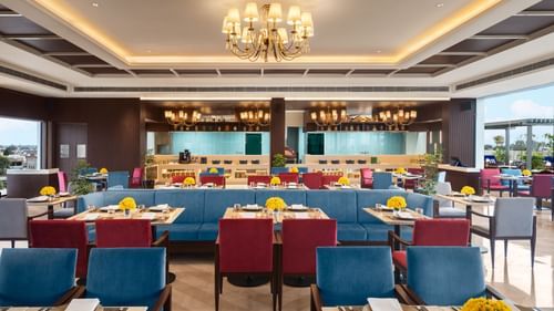 A brightly lit dining room at Sarovar Portico, Hanumangarh, with blue and red chairs, and tables.