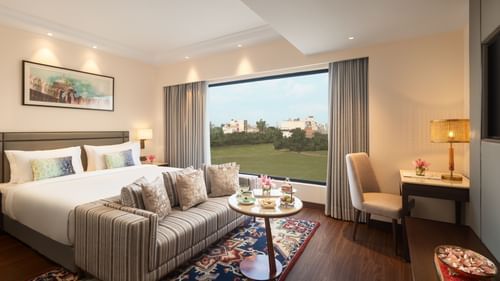 A suite at Sarovar Portico, Hanumangarh, with a double bed, a sofa, a window with a view, and a table.