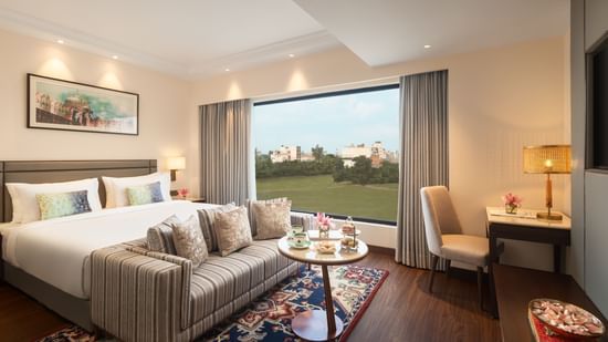 A suite at Sarovar Portico, Hanumangarh, with a double bed, a sofa, a window with a view, and a table.