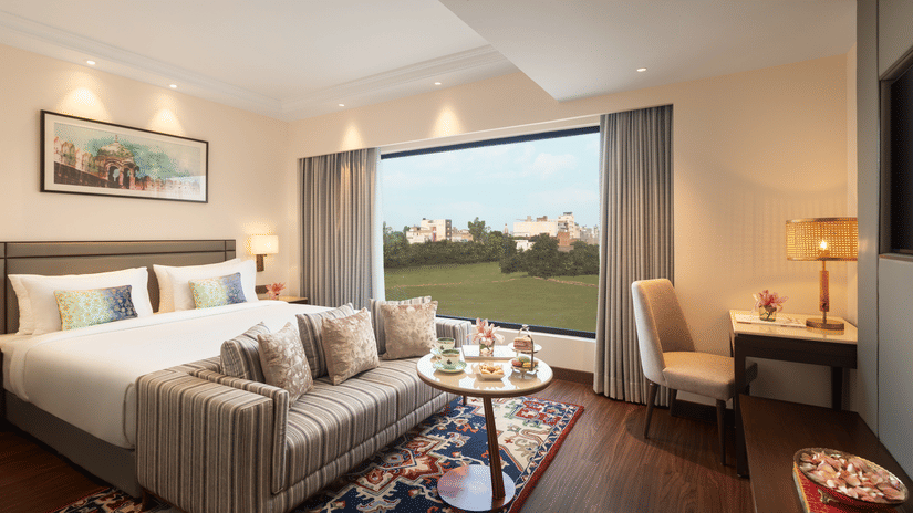 A suite at Sarovar Portico, Hanumangarh, with a double bed, a sofa, a window with a view, and a table.