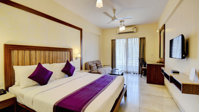 Deluxe King Room with a king size bed, seating area, and balcony door at VITS Lonavala.