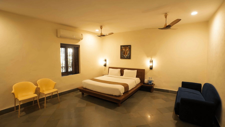 A view of a bedroom at Adamo The Village with a cosy bed, a two-seating sofa, 2 armchairs, and a small window.