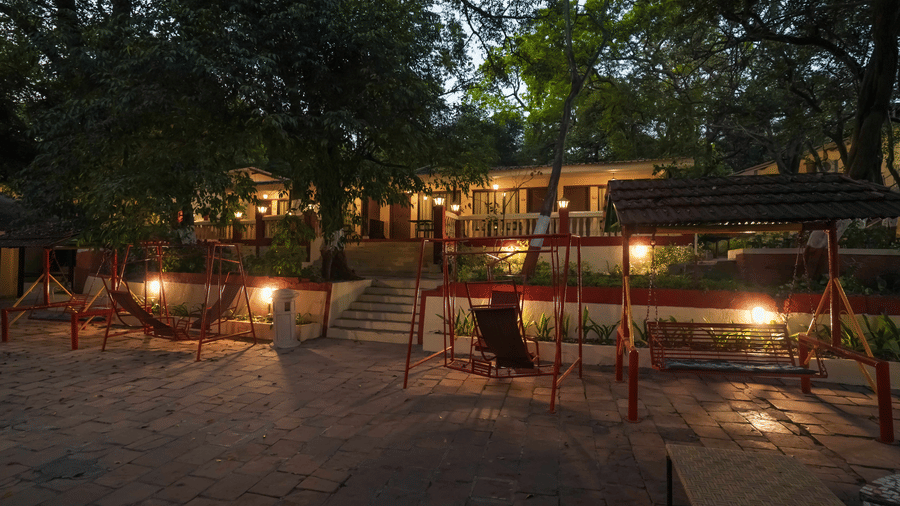 An evening view of the outdoor facade at Adamo The Village featuring a play area, ambient lighting, and a small staircase leading to the cottage.