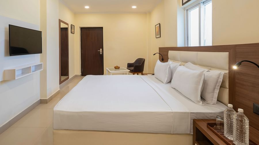 Executive Room featuring a double bed with white bedding, a dark armchair and a small table in the background, and a wall-mounted television at Clarks Inn, Near Kainchi Dham.