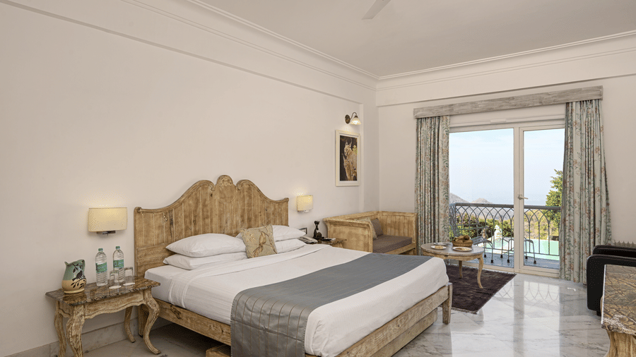 Superior Room with Balcony at Fateh Safari Resort, Kumbhalgarh featuring a double size bed, a bedside table with water bottles, a sofa with centre table, and a balcony with plunge pool with a view of the hill.
