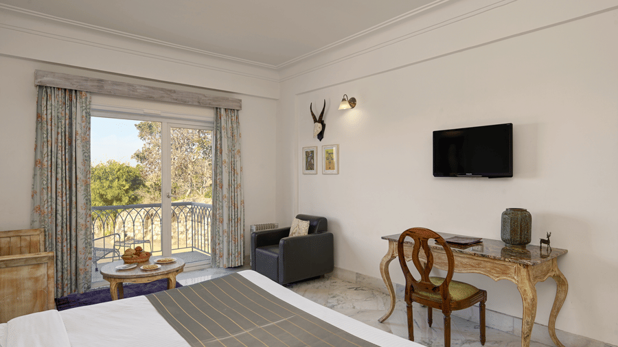 Superior Room with Balcony at Fateh Safari Resort, Kumbhalgarh featuring a flat TV screen, workstation with chair and desk, a sofa chair, centre table, and an attached balcony.