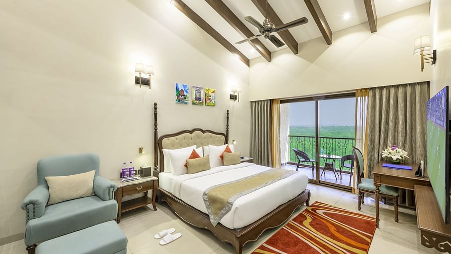 a suite in candolim featuring high ceilings, a king size bed, a blue armchair, a work desk, a flat screen television and a balcony - Golden Tulip, Candolim, Goa