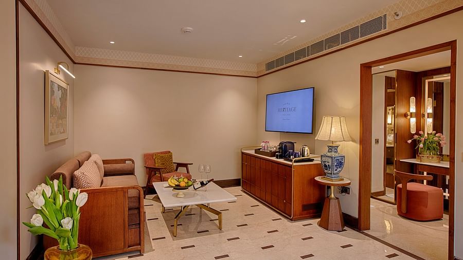 A luxurious suite featuring a cosy seating area, a large flat-screen TV, stylish marble flooring, a wooden centre table, and soft ambient lighting