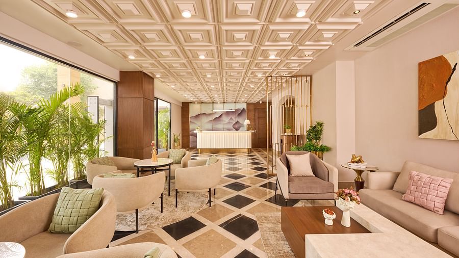 A spacious and well-lit hotel lobby features comfortable armchairs and sofas arranged on a geometrically patterned floor, with large windows overlooking greenery. - Iris Sarovar Portico, Sector 85, Gurugram