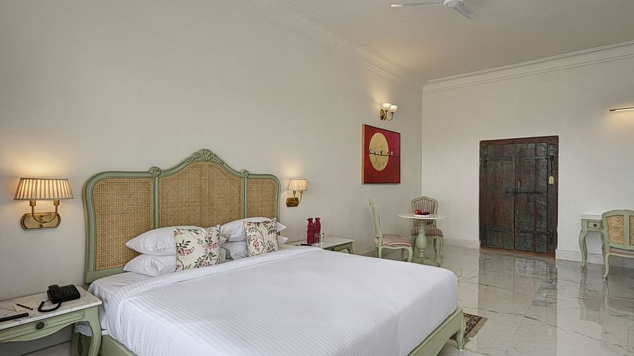 Overview of a well-lit Plunge Pool Suite at Khas Mahal by Fateh Collection, Udaipur featuring a bed, seating area, and a large window with a view.