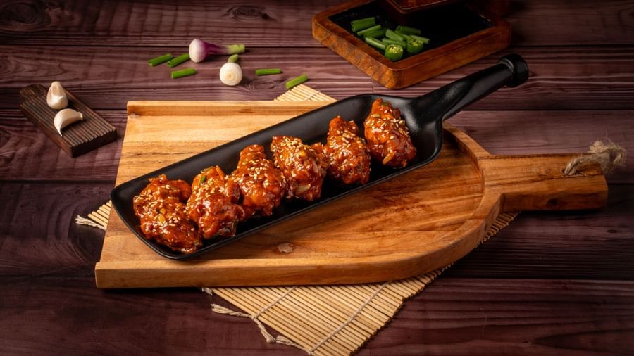 A plate shaped like a bottle holds chicken wings, served on a wooden board with a small bowl of sauce and vegetables on the side.