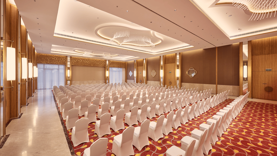 Large function hall at Prachi Sarovar Premiere, Bhubaneswar, filled with rows of chairs set up on patterned carpet under bright ceiling lights.