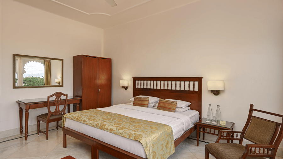 Elegant room with king bed, wooden furniture, flat-screen TV, and warm ambiance at Ram Pratap Palace, Udaipur.
