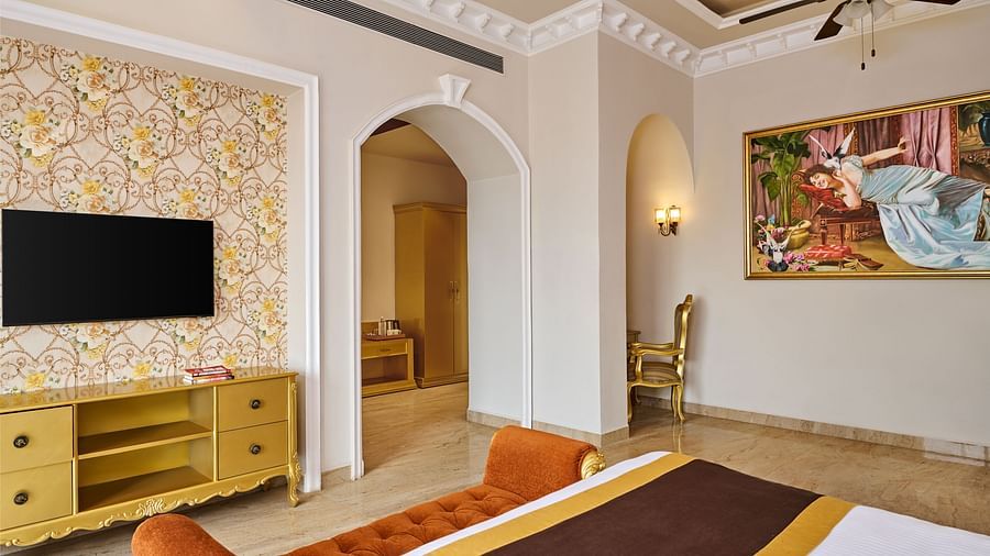 a painting, a bedside bench, a television, and a double bed in the PREMIER ROOM - Royal Kingdom Sarovar Portico, Pilibhit