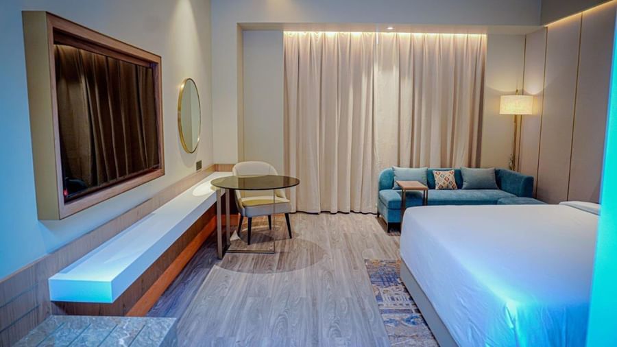 A wall-mounted television, a double bed, a couch, and a work desk in a Hargeisa hotel room - Serene Sarovar Premiere Hargeisa