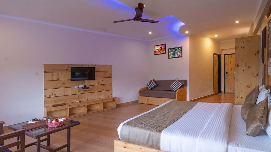 Spacious bedroom with a king bed, table , TV and wooden floor at The Tattwaa Corbett Spa & Resort.