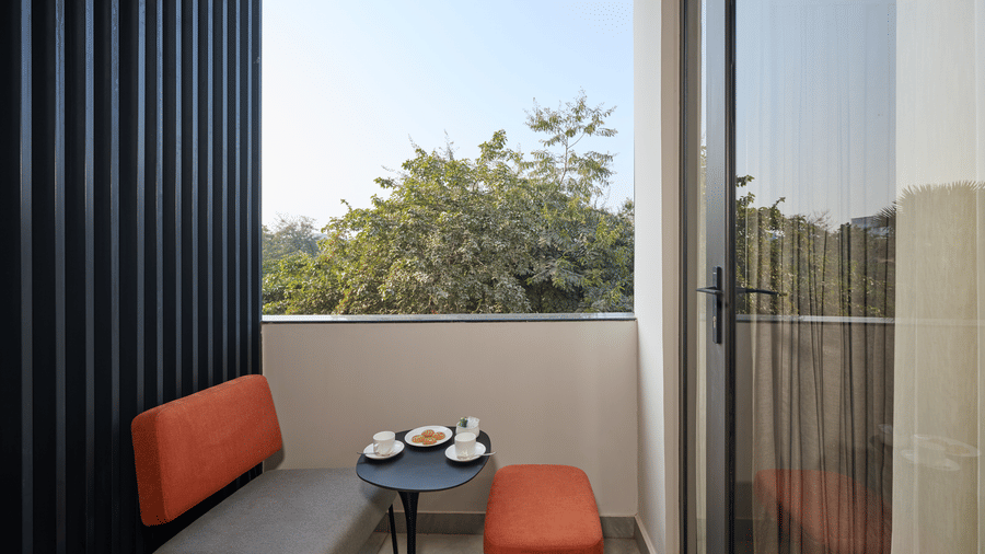 Close-up of a Tulip Inn Gurugram balcony showing outdoor seating with cushions next to a coffee table.