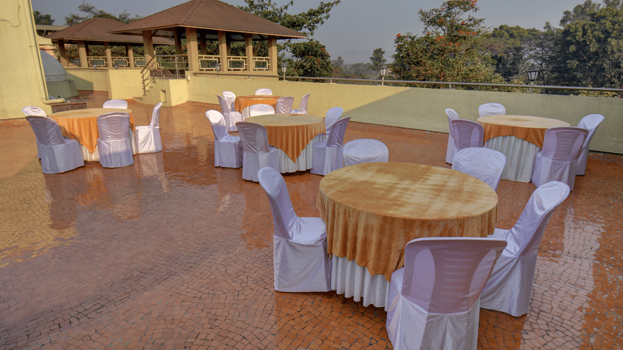 Terrace dining setup with round tables and white chair covers overlooking scenic hills at VITS Lonavala.
