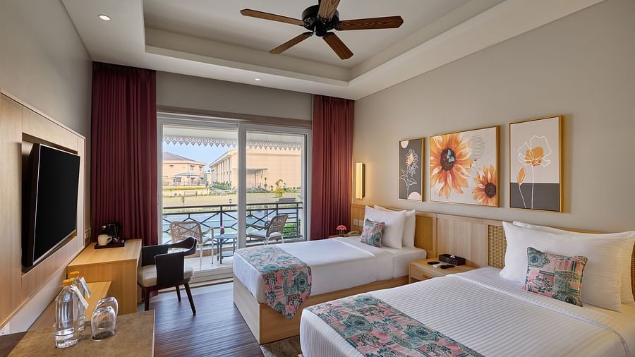 A hotel room featuring two twin beds with floral runners, a desk, a TV, and a view of a body of water through a sliding glass door -  Voyage The Solitaire Bliss.