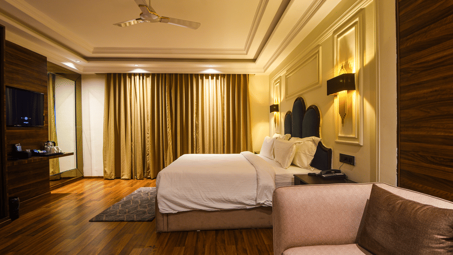 Villa room at Wedlock Greens Hotel & Resort, Dhanbad featuring a king size bed, a sofa, a flat TV screen, a ceiling fan, a tea and coffee maker with glasses.