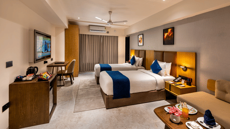 Elegantly furnished deluxe room with a king-sized bed, blue accent pillows, and warm lighting at Lords Studio Inn, Jamnagar.